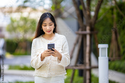 Quadro em tela Asian lady using mobile phone for texting message while walking along the modern