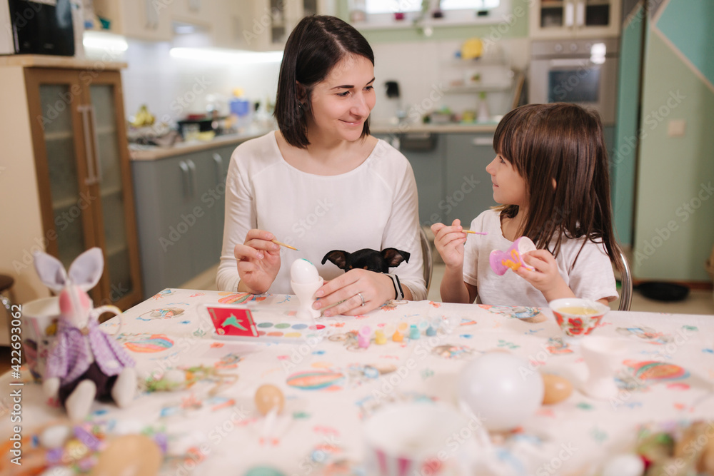 Little girl with her mom preparing for easter and print eggs. They are sitting by the table and have fun