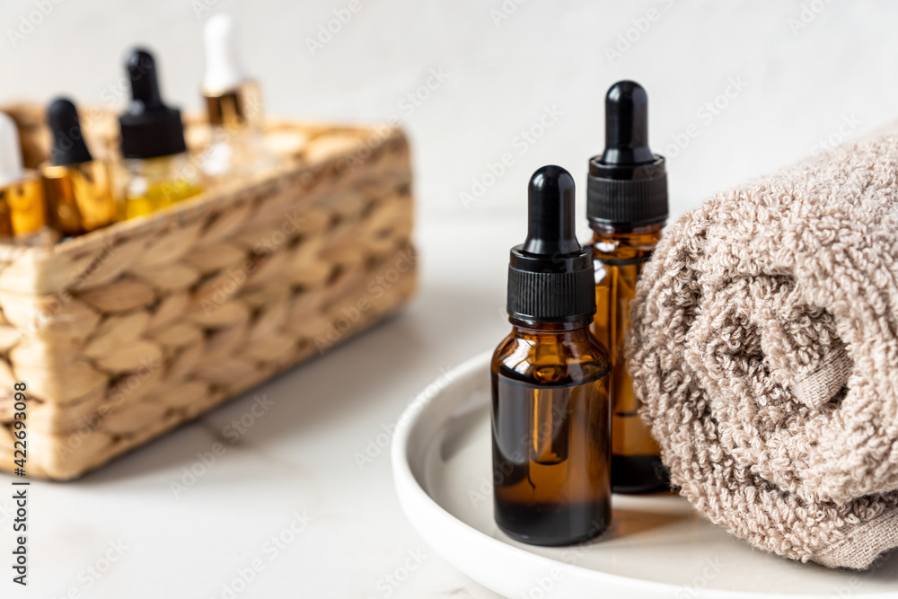 set of different bottles with beauty serum, hyaluronic acid and vitamins on wooden tray with towel. Home spa concept