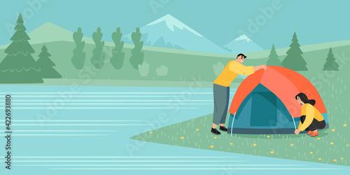 A young couple of tourists sets up a tent on the shore of a beautiful mountain lake.