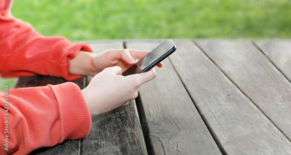 Close-up, woman's hand holding phone in front of blurred green background, hands on wooden table