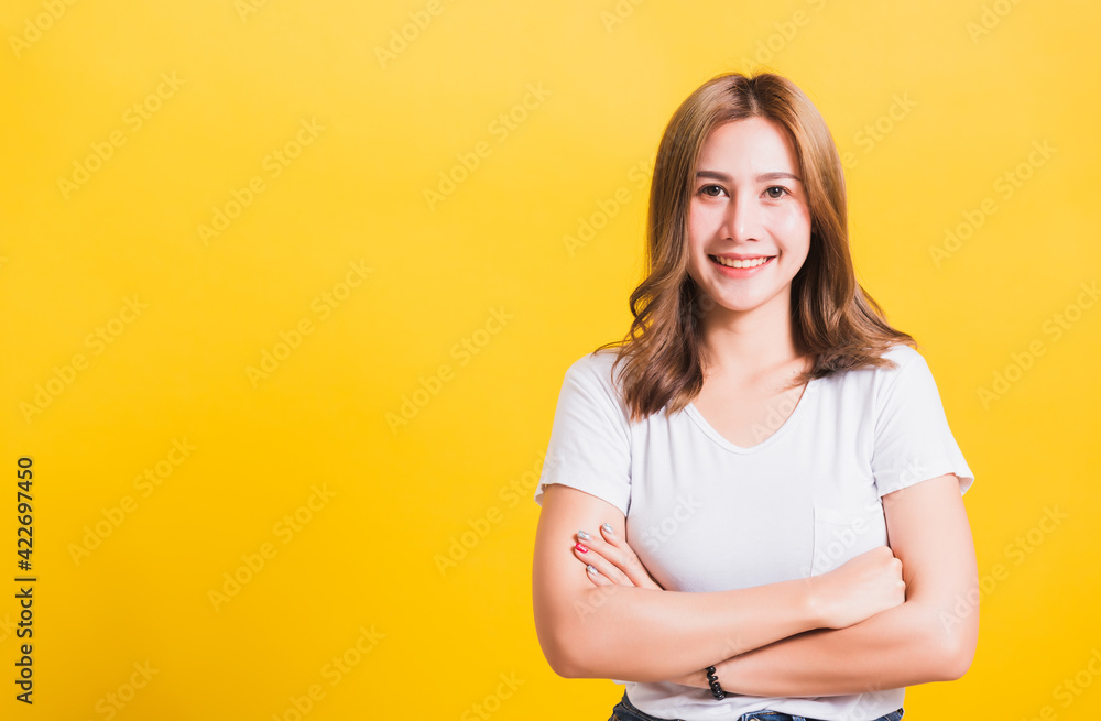 Asian Thai happy portrait beautiful cute young woman standing wear t-shirt her smile confidence with crossed arms looking to side up isolated, studio shot on yellow background and copy space Asian Thai happy portrait beautiful cute young woman standing wear t-shirt her smile confidence with crossed arms looking to side up isolated, studio shot on yellow background and copy space