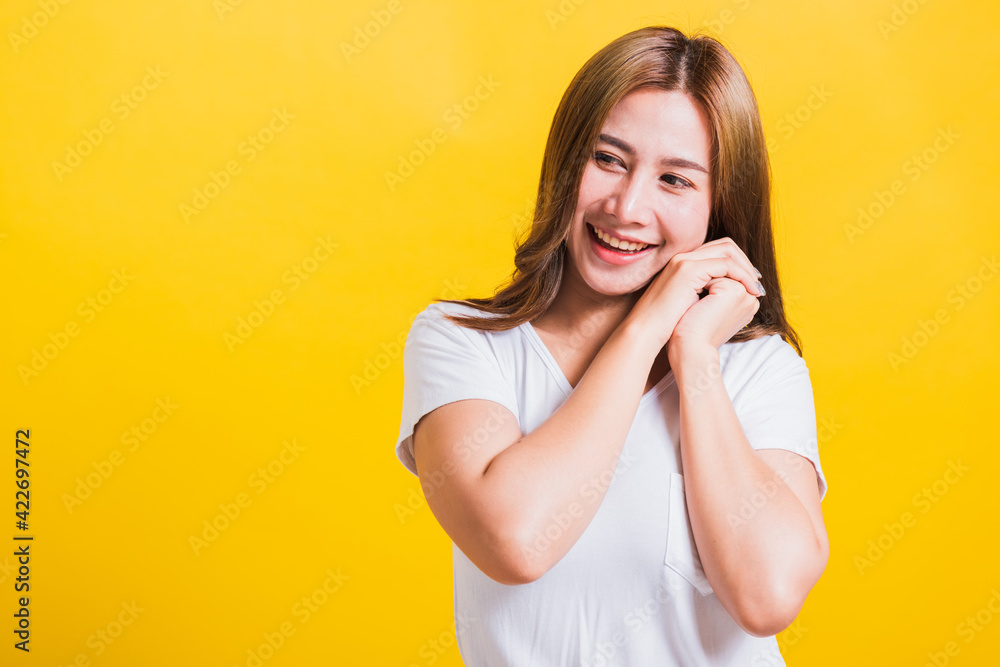 Portrait Asian Thai beautiful happy young woman smiling, screaming excited keeps two hands together near the face and looking to side, studio shot isolated on yellow background, with copy space Portrait Asian Thai beautiful happy young woman smiling, screaming excited keeps two hands together near the face and looking to side, studio shot isolated on yellow background, with copy space