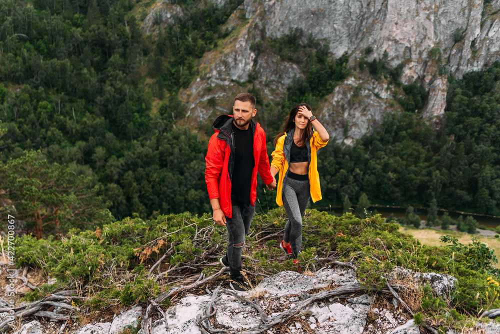 A couple in love on a rock admires the beautiful views. A man and a woman on a rock. A couple in love travels. A walk in the mountains. Couple traveling through the mountains. Hiking. Copy space