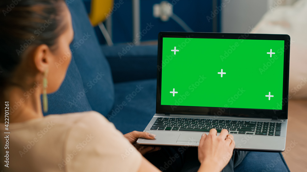 Woman sitting on couch in cozy living room working on laptop computer with mock up green screen chroma key display. Freelancer using isolated pc, browsing on internet for social media advertising Woman sitting on couch in cozy living room working on laptop computer with mock up green screen chroma key display. Freelancer using isolated pc, browsing on internet for social media advertising