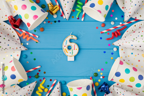 Top view photo of birthday candle for cake topper number six in the middle of birthday composition and party accessories on isolated blue wooden table background