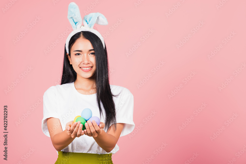 Happy Easter concept. Beautiful young woman smiling wearing rabbit ears holding colorful Easter eggs gift on hands, Portrait female looking at camera, studio shot isolated on pink background Happy Easter concept. Beautiful young woman smiling wearing rabbit ears holding colorful Easter eggs gift on hands, Portrait female looking at camera, studio shot isolated on pink background
