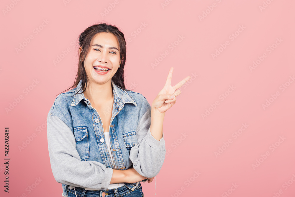 Asian happy portrait beautiful cute young woman wear denim smile stand show finger making v-sign victory sign gesture side away look to camera studio shot isolated on pink background with copy space Asian happy portrait beautiful cute young woman wear denim smile stand show finger making v-sign victory sign gesture side away look to camera studio shot isolated on pink background with copy space