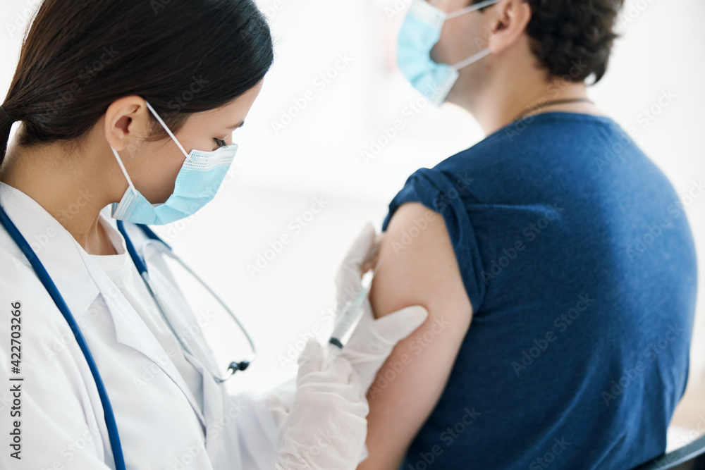 female nurse in a medical mask injects a vaccine into the shoulder of a patient vaccination female nurse in a medical mask injects a vaccine into the shoulder of a patient vaccination