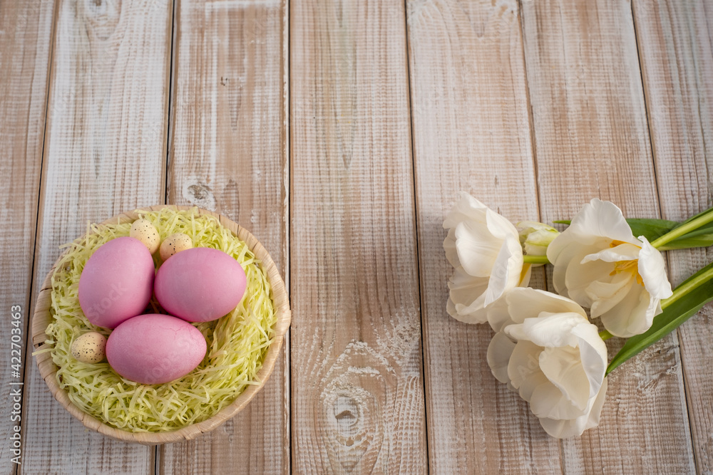 Easter eggs in a nest on a wooden background with white tulips