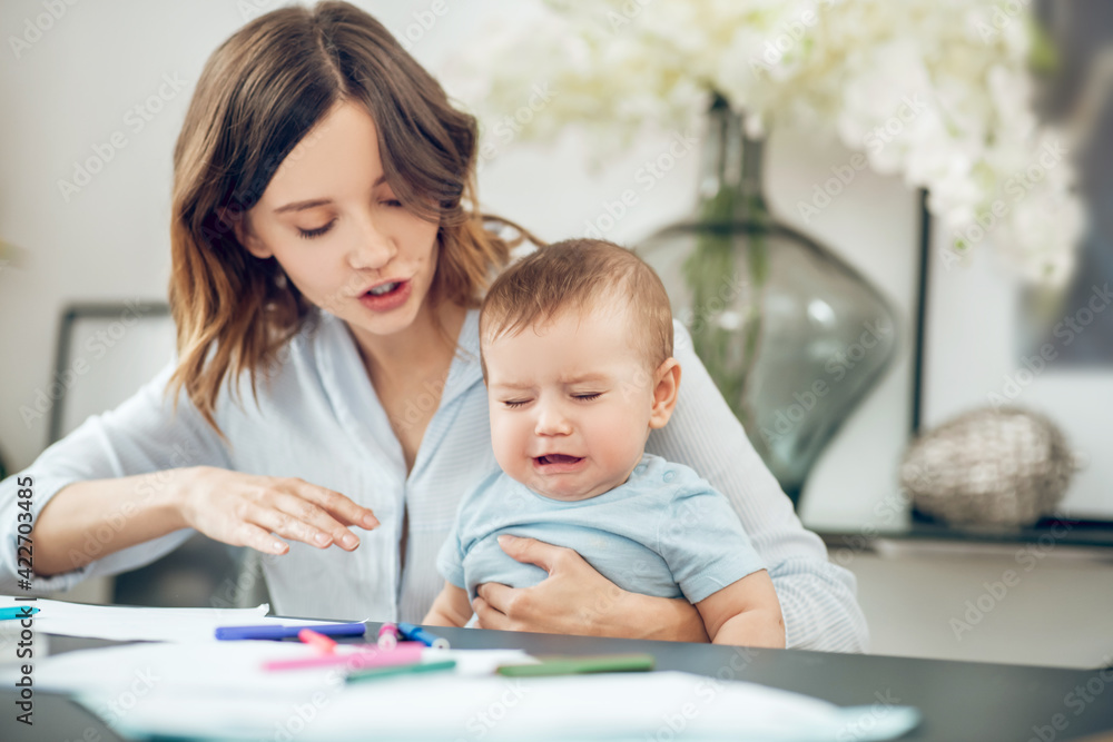 Young mother soothing crying baby sitting at table Young mother soothing crying baby sitting at table