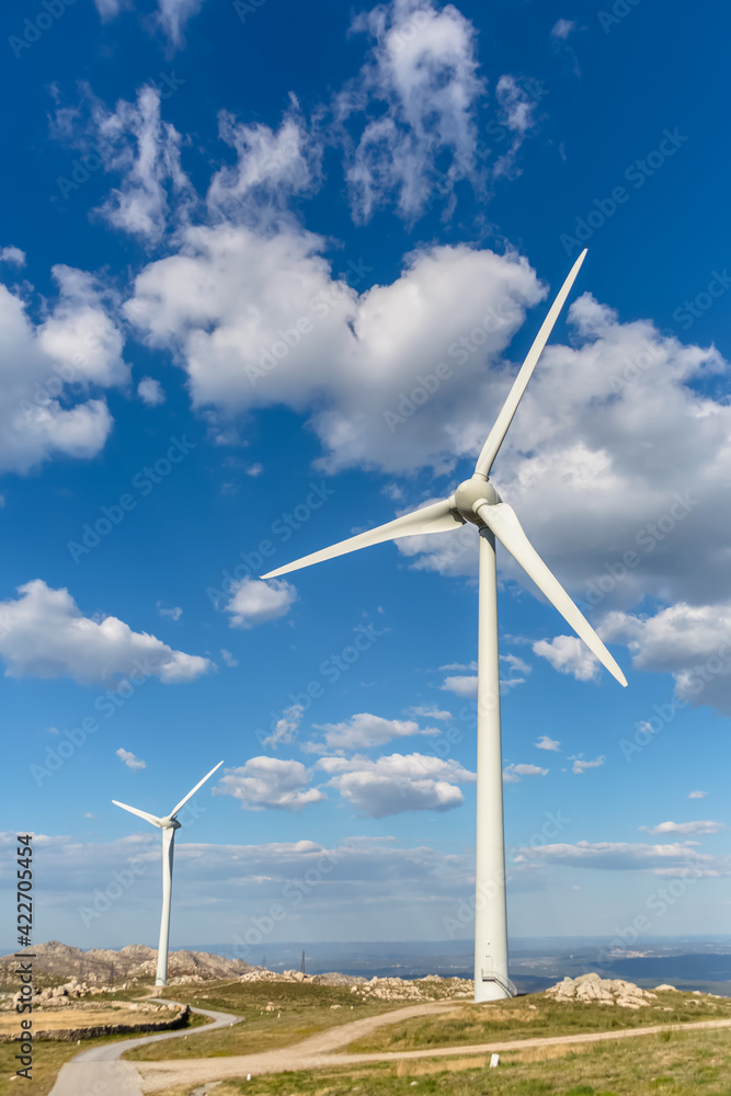 View of a wind turbines on top of mountains, dirt road and wild nature and landscape View of a wind turbines on top of mountains, dirt road and wild nature and landscape