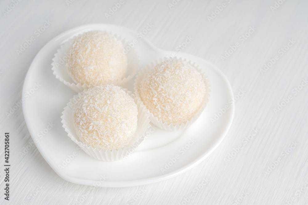 Coconut organic sweet truffles or homemade nut vegetarian energy balls served in heart shaped plate on white wooden background at kitchen ready to eating for breakfast. Horizontal orientation image