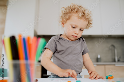Portrait of a pre-school girl sitting at her kitchen table playing with plasticine. The cute lovely girl is spending his afternoon free time at home.