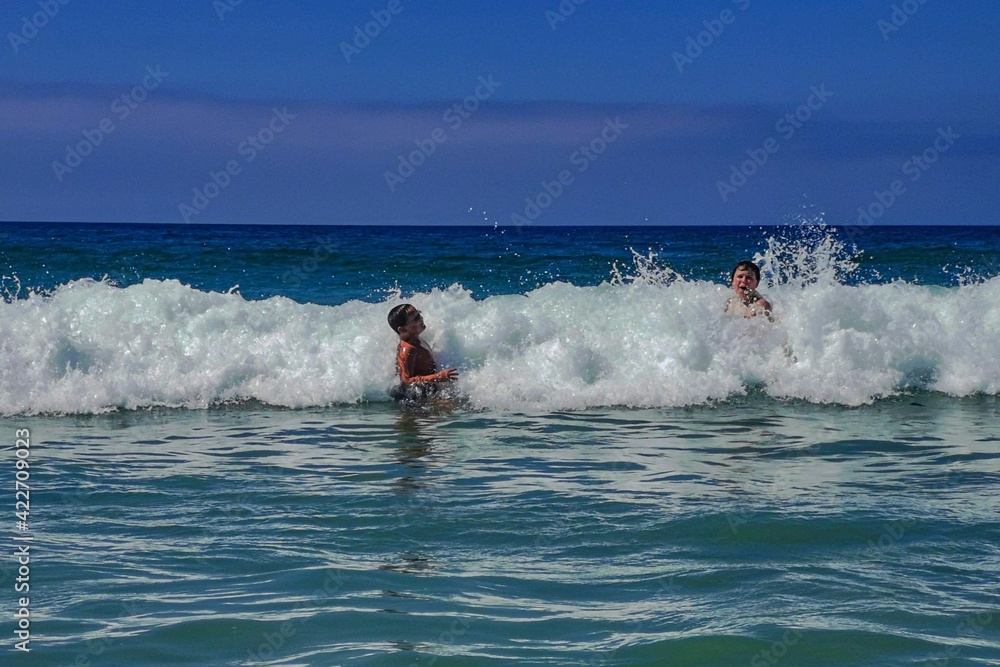 Naklejka premium Niños saltando olas en la playa