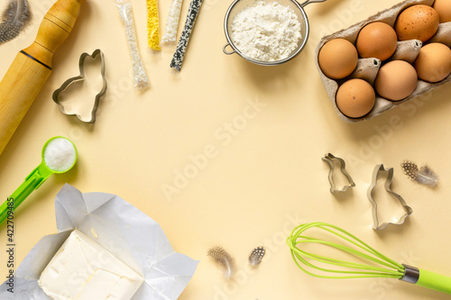 Frame of ingredients for easter baking and kitchen utensil. Flour, eggs, butter and sweet sprinkles on beige background