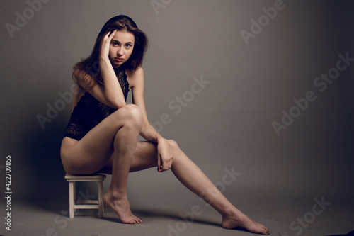 Young brunette female in black bra jeans and leather jacket over grey background