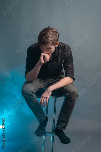 Frustrated young man sits on a bar stool amid blue smoke