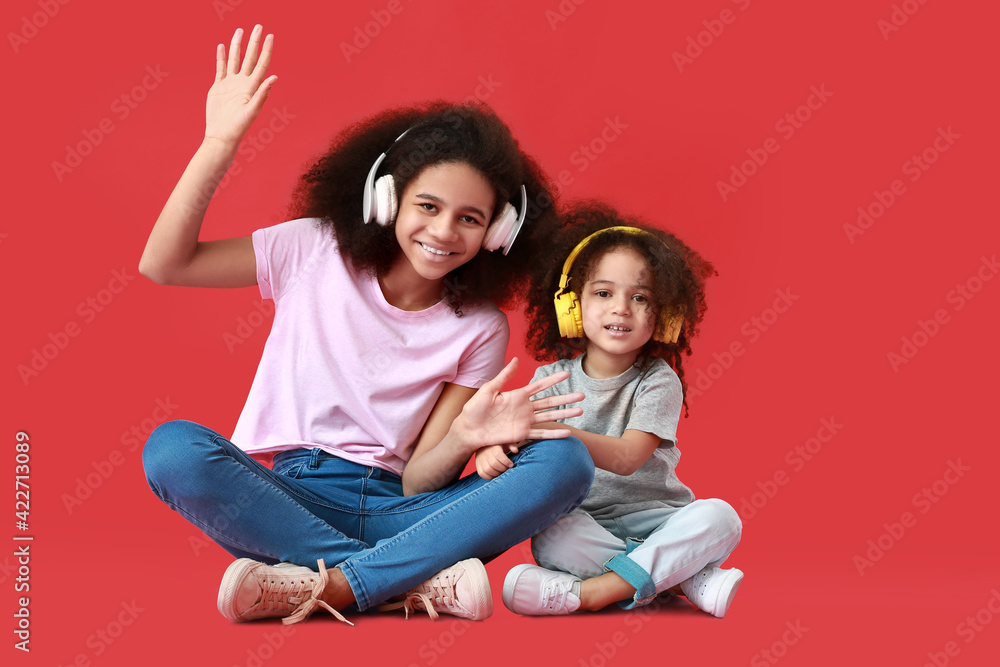 Portrait of cute African-American sisters listening to music on color background
