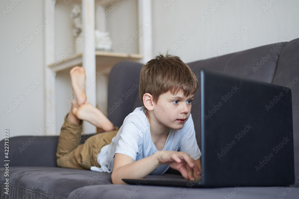 Boy sitting at home on the sofa and holding a laptop in his hands, gadget addiction concept, virtual online learning Boy sitting at home on the sofa and holding a laptop in his hands, gadget addiction concept, virtual online learning
