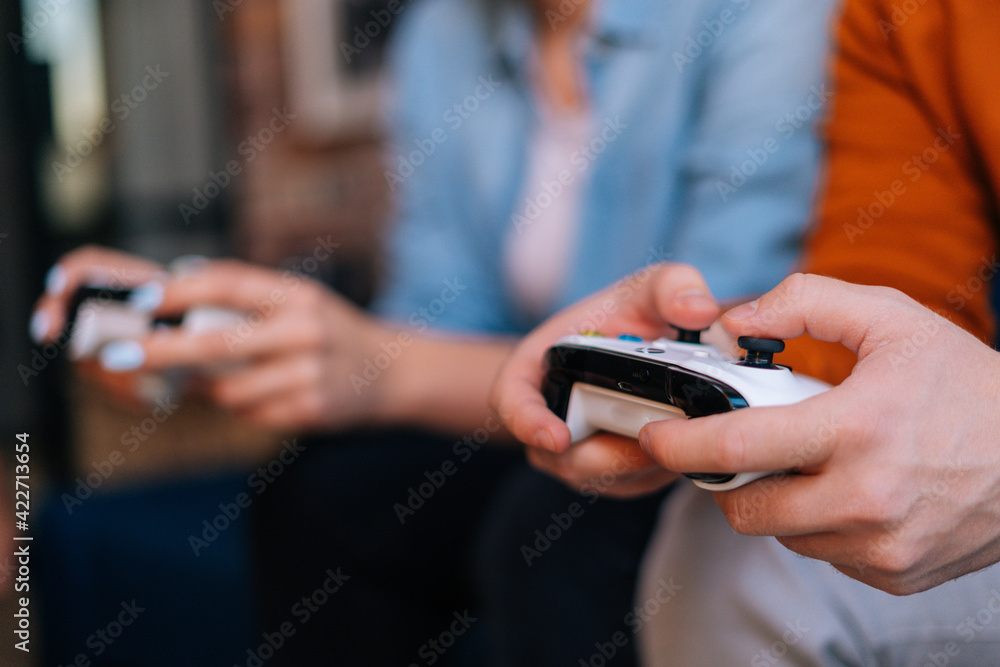 Close-up view of young couple holding controllers and playing video games on console sitting together on sofa at cozy living room. Concept of leisure activity of lovers at home.