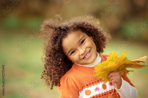 Cute afro girl smiling broadly outdoors and enjoying autumn day in park.
