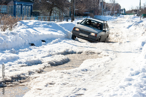A car on a road with deep puddles from melting snow at the end of March