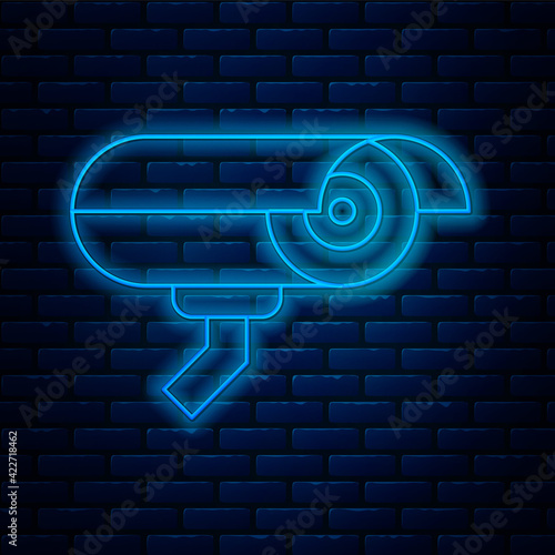 Glowing neon line Security camera icon isolated on brick wall background. Vector