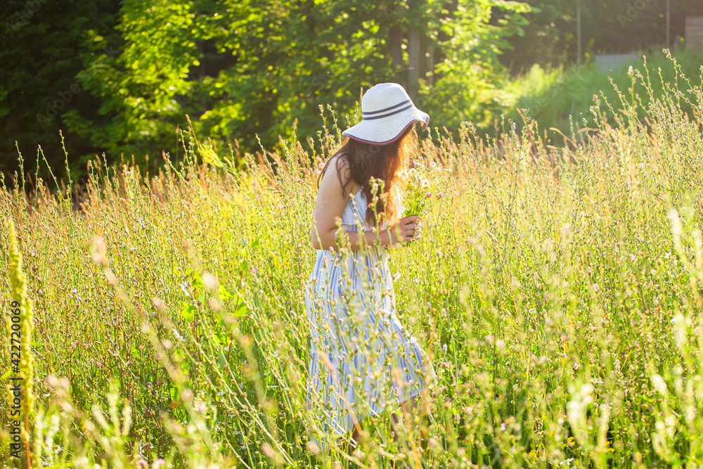 Happy young woman with long hair in hat and dress walking through the summer forest on a sunny day. Summer joy concept