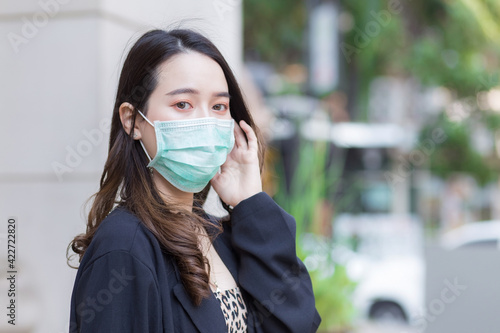 Asian beautiful woman in black coat is wearing a medical face mask to protect respiratory system from Coronavirus-19 (COVID-19) infection in health care,pollution PM2.5 and new normal concept..