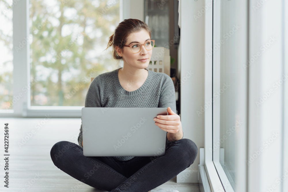 Thoughtful young woman sitting cross egged on the floor with laptop Thoughtful young woman sitting cross egged on the floor with laptop