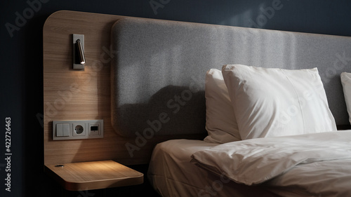 Close-up fragment of bedroom with empty bedside table, reading lamp and a USB socket in modern interior​ design home or hotel. Soft pillow and blanket, stylish comfortable furniture. Sun shadows. photo