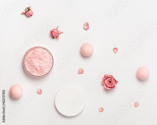 Rose scented sea salt in jar with cap and rose flowers. Cosmetic product top view, trend pink pastel colored