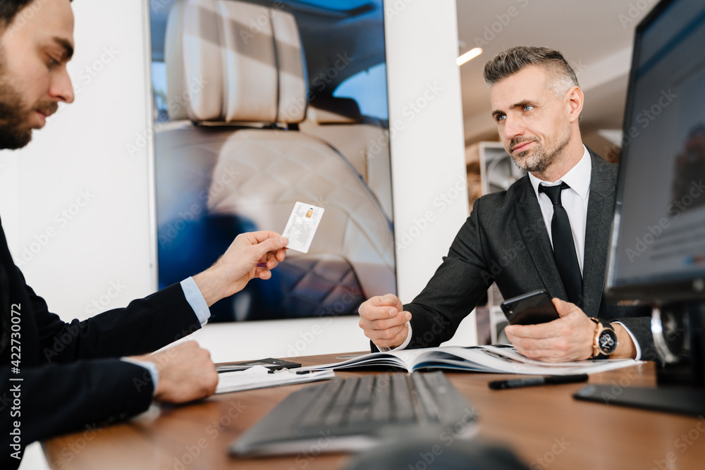 Mature man using credit card while paying his new car in office Mature man using credit card while paying his new car in office