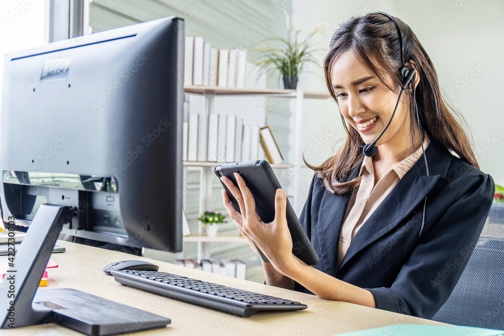 Asian beautiful young girl call center operator in headset answering calls and using tablet at call center, She's talking on the phone Asian beautiful young girl call center operator in headset answering calls and using tablet at call center, She's talking on the phone