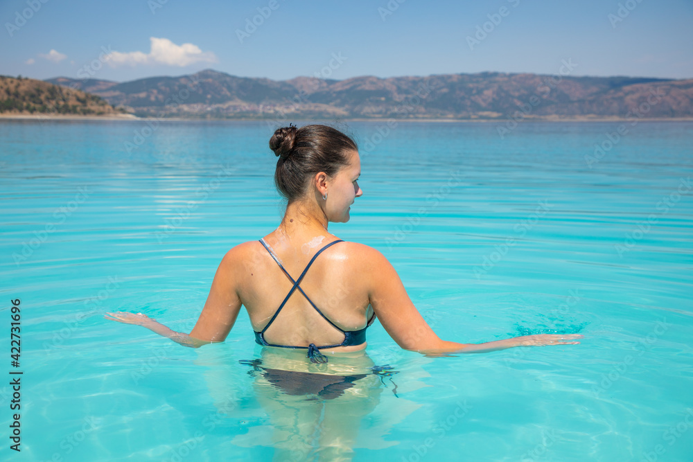 A young sexy female in swim suit is swimming in turquoise crater lake Salda Golu, Turkey