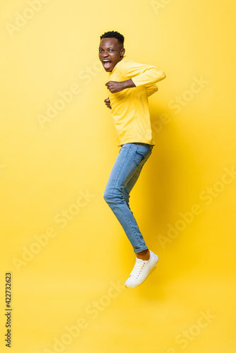 Young cheerful excited African man jumping with clenching hands on isolated yellow studio background