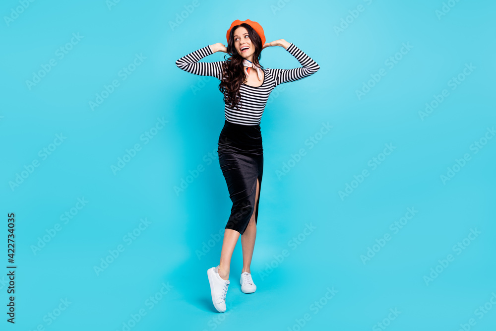 Full size photo of pretty girl hands touch beret look empty space toothy smile isolated on blue color background Full size photo of pretty girl hands touch beret look empty space toothy smile isolated on blue color background