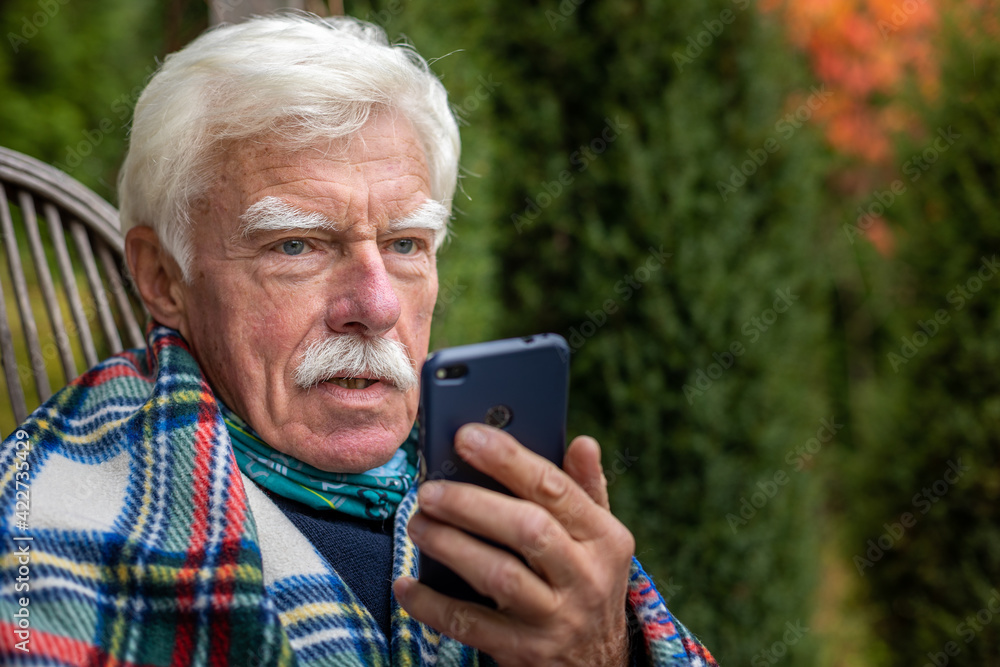 An elderly gentleman is having a phone call. Senior man sitting in the rocking chair during his smartphone conversation. Mature man using his cellular on the veranda. An elderly gentleman is having a phone call. Senior man sitting in the rocking chair during his smartphone conversation. Mature man using his cellular on the veranda.