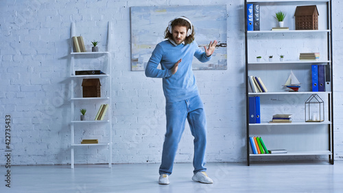full length view of young businessman in wireless headphones dancing in modern office