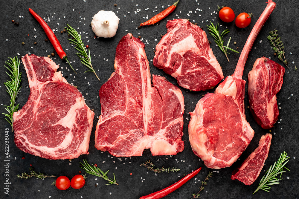 Variety of raw beef steaks for grilling with spices on stone background