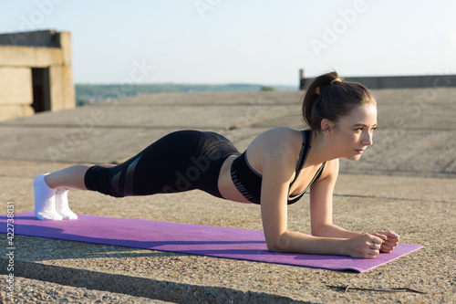 A young slim athletic girl in sportswear performs a set of exercises.