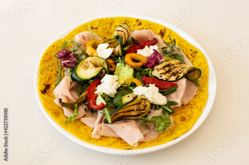 Turmeric flatbread with ham cheese and grilled vegetables on a white background.