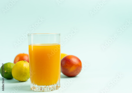 Glass of yellow juice with fruits on a blue background