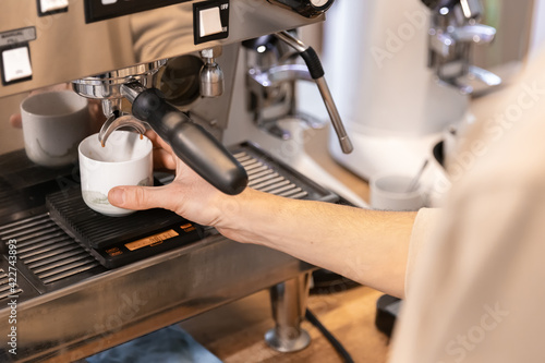 A man makes a fresh espresso in a coffee maker. The barista prepares a hot drink for the clients.