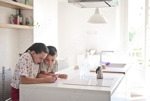 two children use a smartphone in the kitchen