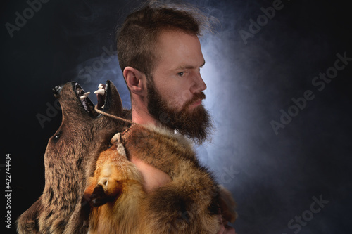 Obraz na plátně Low key portrait of a bearded war shaman in bearskin with an ancient ax in his hands