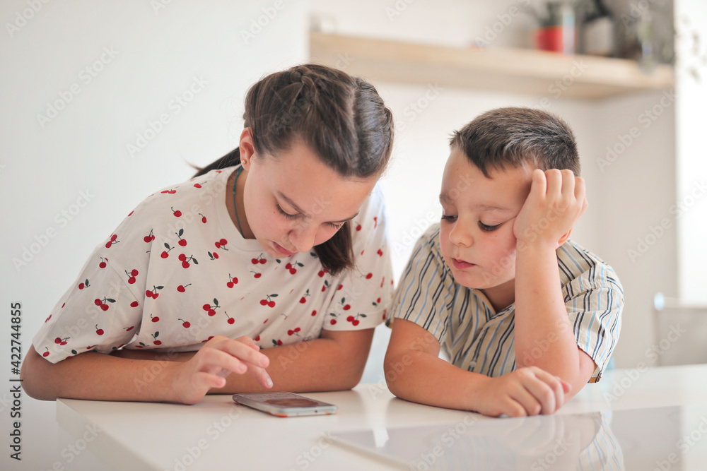 two children use a smartphone in the kitchen two children use a smartphone in the kitchen