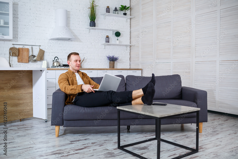 A young successful man is sitting at home on the couch with a laptop and working. Remote work during quarantine. A young successful man is sitting at home on the couch with a laptop and working. Remote work during quarantine.