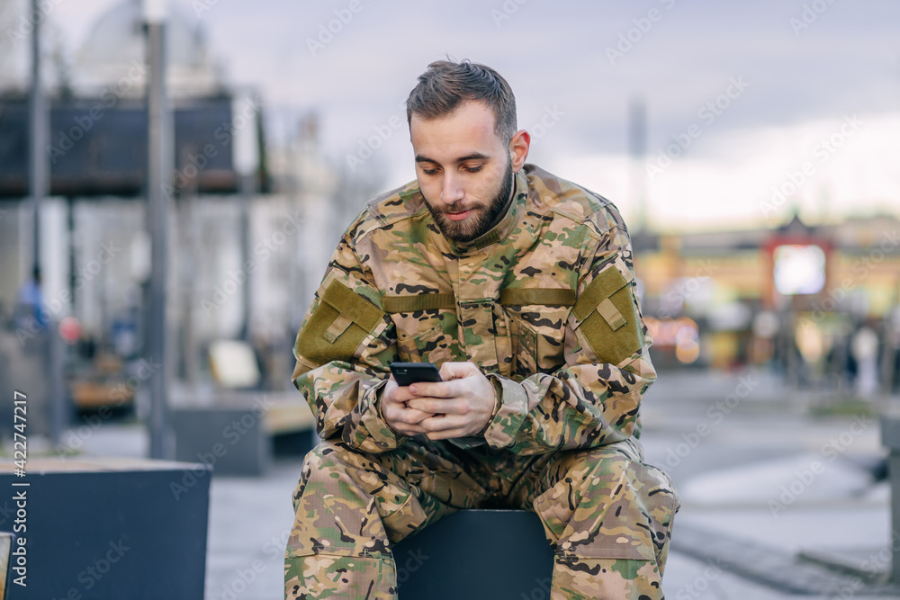 A military soldier sits on a bench at a bus stop waiting for a b A military soldier sits on a bench at a bus stop waiting for a b